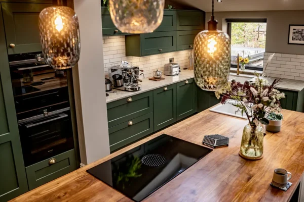Handcrafted green painted kitchen with wooden island worktop, pendant lighting and premium appliances.